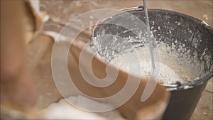 Construction worker man stirs the mixture in the bucket construction for alignment and putty walls of the apartment with