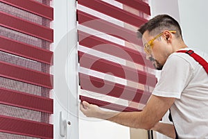 Construction worker man in a uniform install blinds on plastic white upvc windows in house