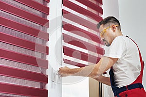 Construction worker man in a uniform installing new window blinds