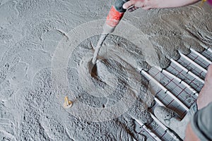 Construction worker pouring concrete on underfloor heating system