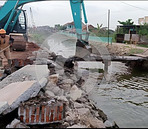 A construction worker operates an excavator to dig a hole in a riverbed