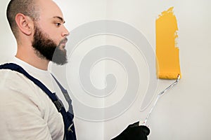 Construction worker and painter using paint roller brush painting of wall with yellow color.