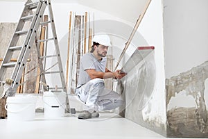 Construction worker plasterer man looks at the spirit level and checks the wall in building site of home renovation with tools and