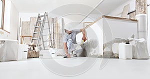 Construction worker plasterer man measuring wall with measure tape in building site of home renovation with tools and building