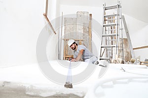 Construction worker plasterer man measuring wall with measure tape in building site of home renovation with tools and building