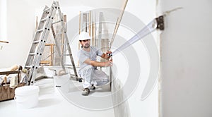 Construction worker plasterer man measuring wall with measure tape in building site of home renovation with tools and building