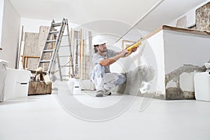 Construction worker plasterer man uses caulking gun in building site of home renovation with tools and building materials on the