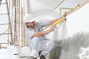 Construction worker plasterer man uses caulking gun in building site of home renovation with tools and building materials on the
