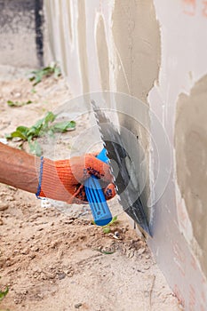 Construction worker plastering a wall and house foundation with trowel.