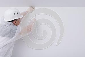 A construction worker in protective clothing and a hard hat, glues paint tape to create a multi-colored interior, on a white wall