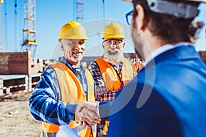 Construction worker in protective uniform shaking hands with businessman