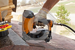 Construction worker putting the asphalt roofing shingles with nail gun on a large commercial apartment building development.