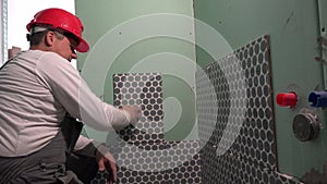 Construction worker with red helmet tiling wall with ceramic tiles