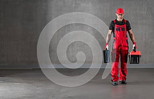 Construction Worker in Red Uniform Walking with Toolboxes in His Hands