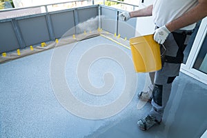 Construction worker renovates balcony floor and spreads chip floor covering on resin and glue coating before applaying water