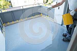 Construction worker renovates balcony floor and spreads chip floor covering on resin and glue coating before applaying water