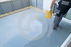 Construction worker renovates balcony floor and spreads chip floor covering on resin and glue coating before applying water