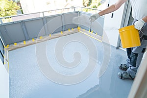 Construction worker renovates balcony floor and spreads chip floor covering on resin and glue coating before applying water