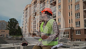 Construction worker resting on building site drinking coffee to go and using smartphone while sitting on jobsite