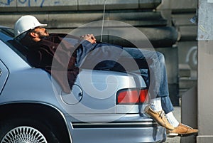 A construction worker resting on his car,