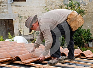 Construction worker on a roof covering it with tiles - roof renovation: installation of tar paper, new tiles