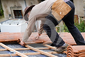 Construction worker on a roof covering it with tiles - roof renovation: installation of tar paper, new tiles