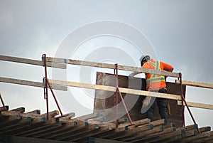 Construction worker on roof metal beams man holding plywood
