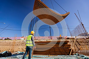 Construction worker with safety helmet at construction site as crane carry bunch of armature