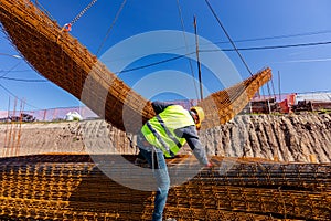 Construction worker with safety helmet at construction site helping crane to manage bunch of armature