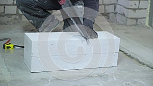 Construction worker sawing aerated concrete block after measuring it