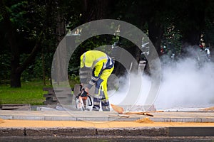 Construction worker sawing brick on the street with dust cloud behind. Urban development