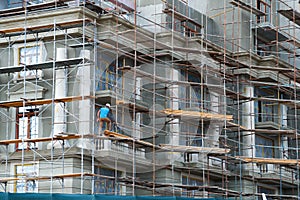 Construction worker is on scaffold, modern building under construction, plastered walls and scaffolding