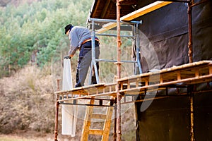 Construction worker on scaffold thermally insulating house, black foil