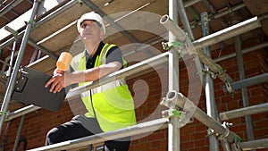 Construction worker on scaffolding with a clipboard and drinking mug of tea or coffee