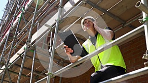 Construction worker on scaffolding with a clipboard and talking on cell phone