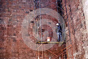 Construction worker on scaffolding working on textured wall