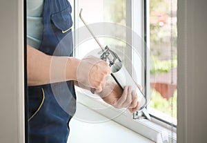 Construction worker sealing window with caulk