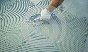 Construction worker spreading tile adhesive on floor