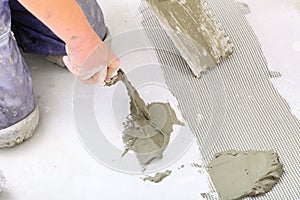 Construction worker is tiling at home, tile floor adhesive