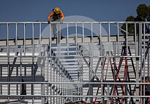 Construction worker on top of steel framing in white hard hat and orange long sleeve shirt