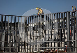 Construction worker on top of steel framing in white hard hat and orange long sleeve shirt