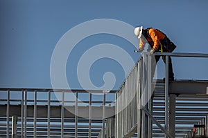 Construction worker on top of steel framing in white hard hat and orange long sleeve shirt