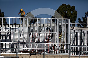 Construction worker on top of steel framing in white hard hat and orange long sleeve shirt