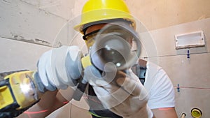 A construction worker uses an electric drill looking into the camera lens. Home renovation concept