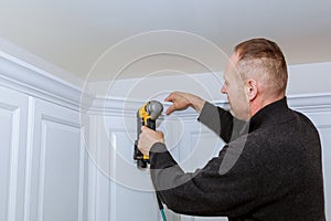 Construction worker using brad nail air gun to Crown Moulding on white kitchen wall cabinets framing trim,