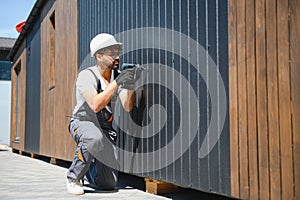 Construction worker using cordless drill installing modular house panel