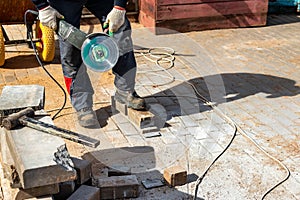 A construction worker using an electric grinder and a diamond cutting disc cuts paving slabs while paving a sidewalk in the