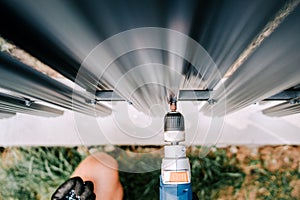 Construction worker using electric screwdriver and drilling holes in metal fence