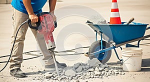 Construction worker using a jackhammer to break up concrete on a sunny day