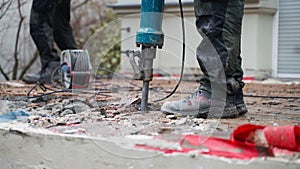 A construction worker using a jackhammer to remove old concrete near the house